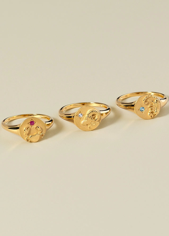 Three gold rings with face designs on a beige background